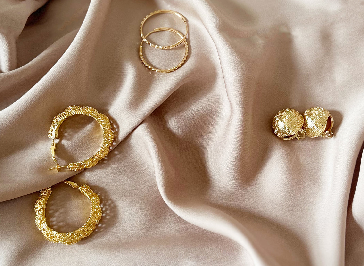 Trois paires de boucles d'oreilles posées sur un tissu en satin