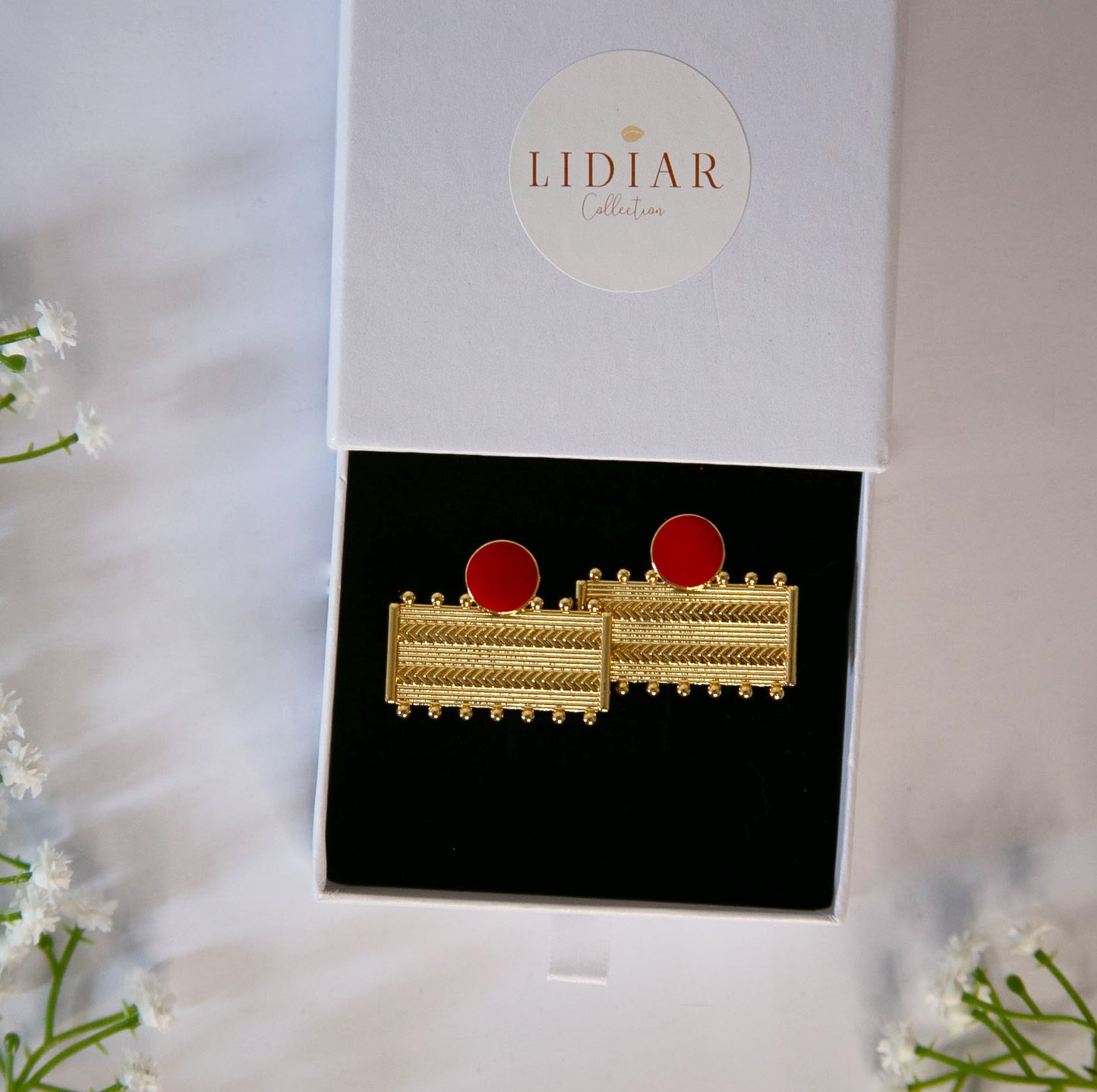 Boucles d'oreilles dorées et rouge, rectangulaires, avec des formes géométriques dans un écrin à bijoux lidiar collection