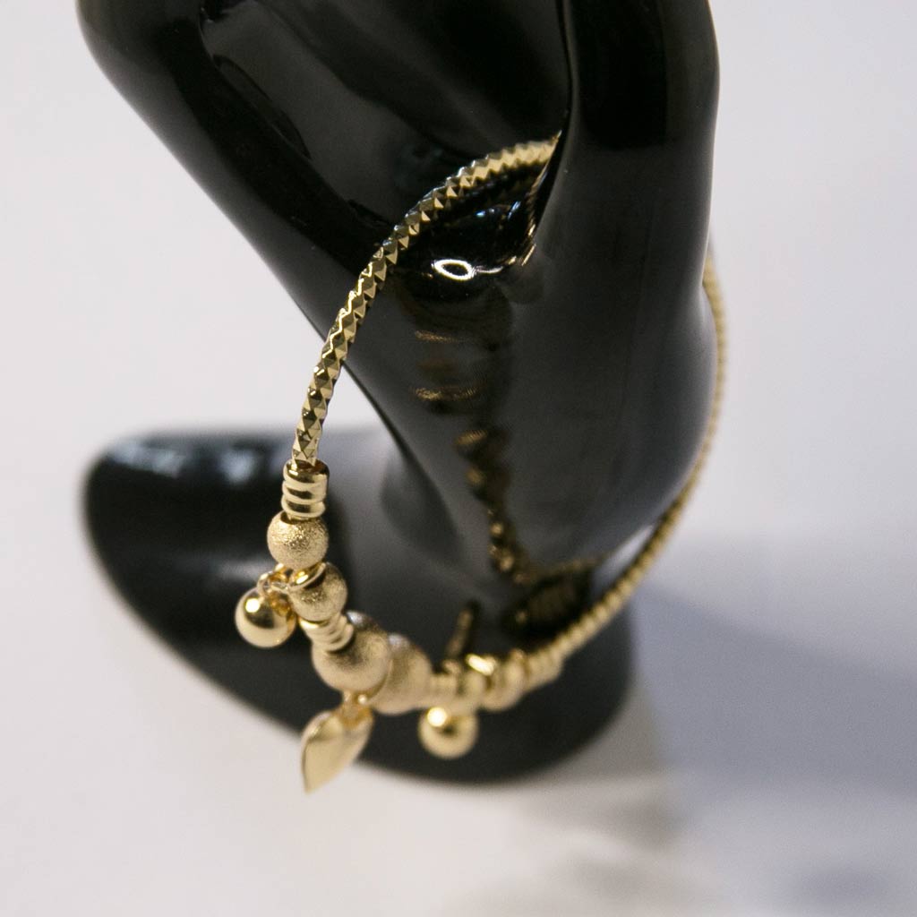 Main de mannequin tenant un bracelet en acier inoxydable, doré, avec un pendentif coeur et des boules