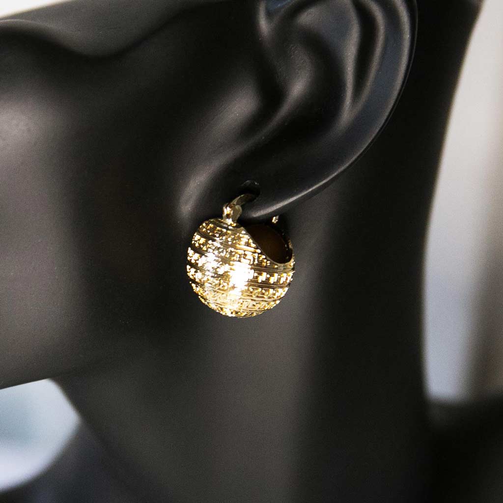 Tête de mannequin portant une boucle d'oreille dorée en forme de boule avec des motifs géométriques
