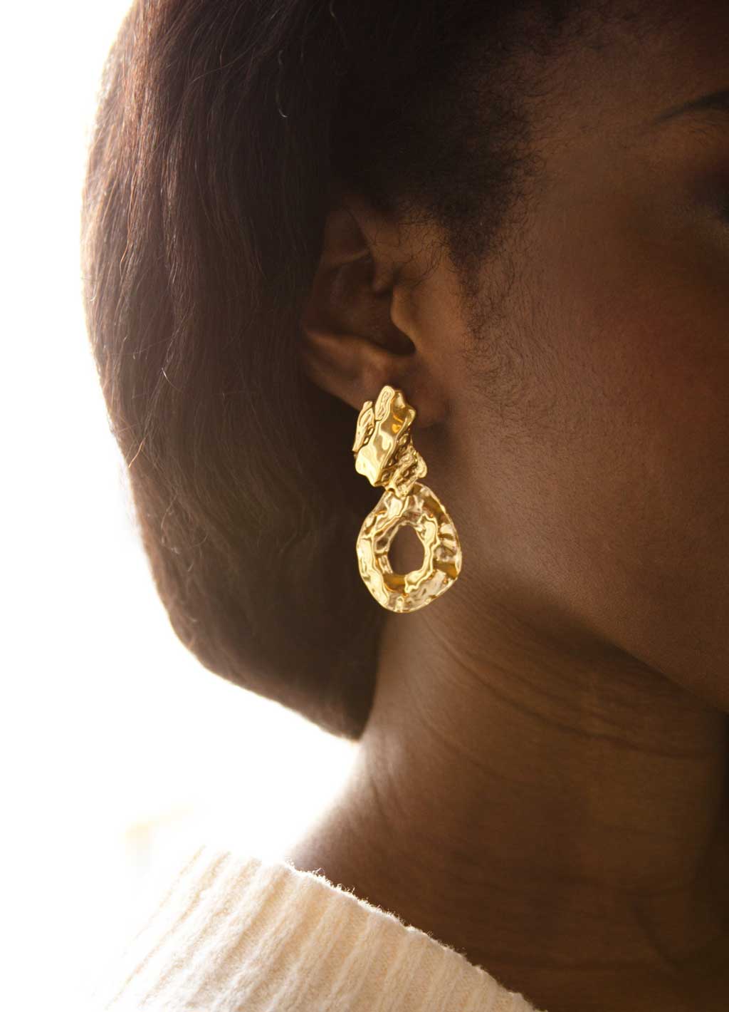 femme portant boucle d'oreille dorée pendentif texture martelée