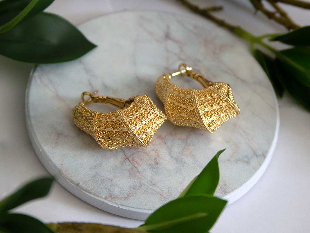 boucles d'oreilles dorée posées sur un plateau en marbre avec des plantes vertes en décoration