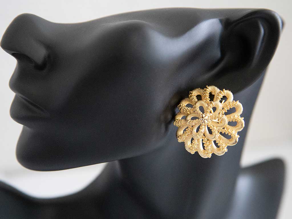 tête de mannequin portant une grosse boucle d'oreilles dorée en forme de fleur