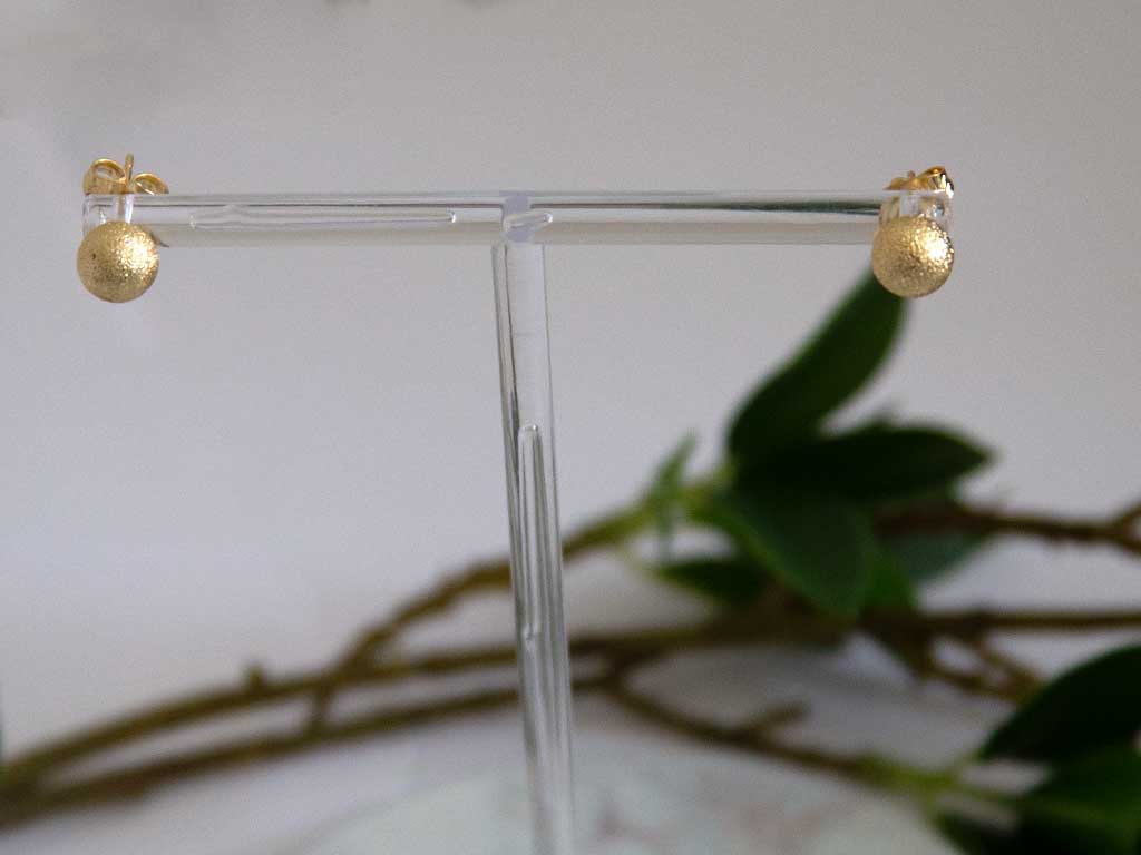 boucles d'oreilles puce dorée sur un présentoir et des plantes vertes en fond