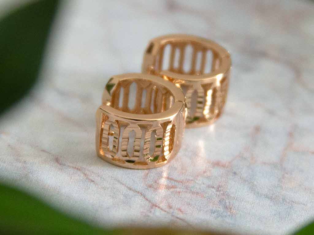 petite boucles d'oreilles huggies dorée posées sur un plateau de marbre avec une décoration de plantes vertes