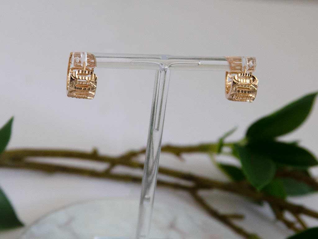 petite boucles d'oreilles huggies dorée posées sur un présentoir avec une décoration de plantes vertes