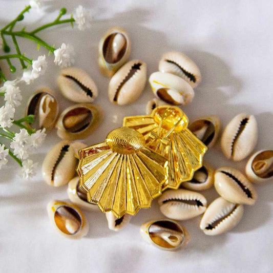 Boucles d'oreilles ethniques, dorées, posées sur des coquillages cauris et des fleures blanches en décor