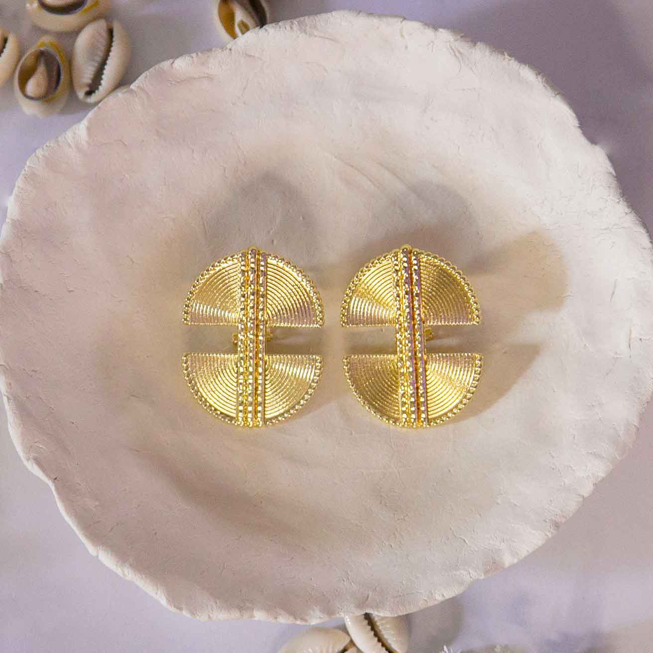 Boucles d'oreilles, style ethnique , dorée posées sur un plateau avec décor de coquillages cauris