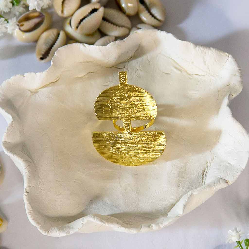 Bague doré, de style ethnique, posée sur un plateau, avec un décor de coquillage cauris et de fleurs blanches
