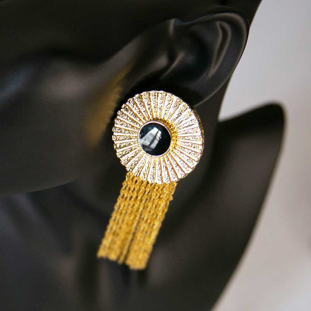 Tête de mannequin portant une boucle d'oreille dorée avec un centre noir et de longues chaines pendantes dorées
