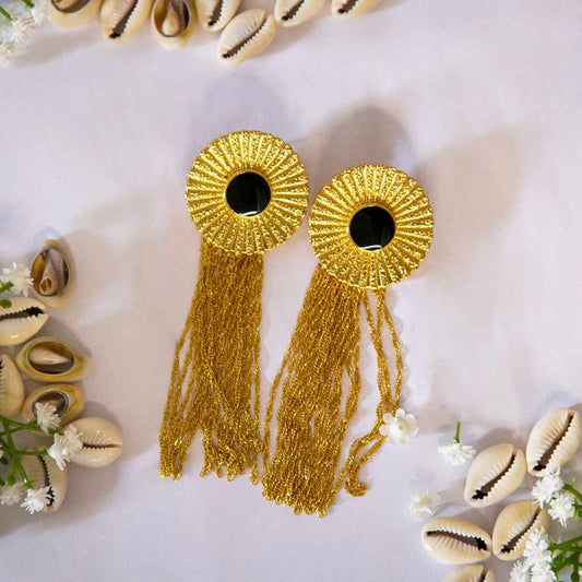 Boucles d'oreilles dorées avec un centre noir et des chaines pendantes dorées, avec un décor de coquillage cauris et des fleures blanches