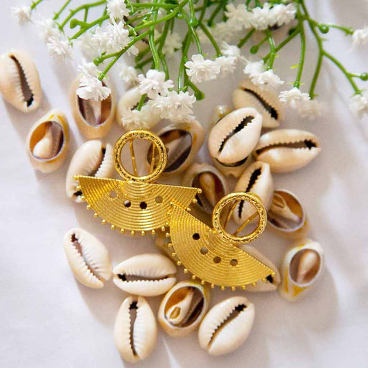 Boucles d'oreilles au style ethnique, dorées en forme de demi rond, posées sur des coquillages cauris et des fleures blanches