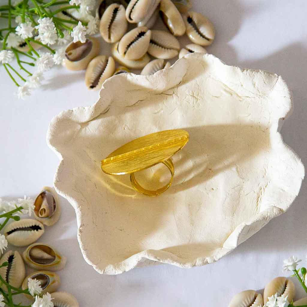 Bague ronde de style ethnique, dorée, posée sur un plateau, avec un décor de cauris et de fleures blanches
