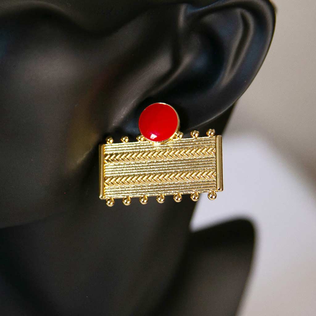Tête de mannequin portant une boucle d'oreilles rectangulaires dorée et rouge avec des motifs géométrique