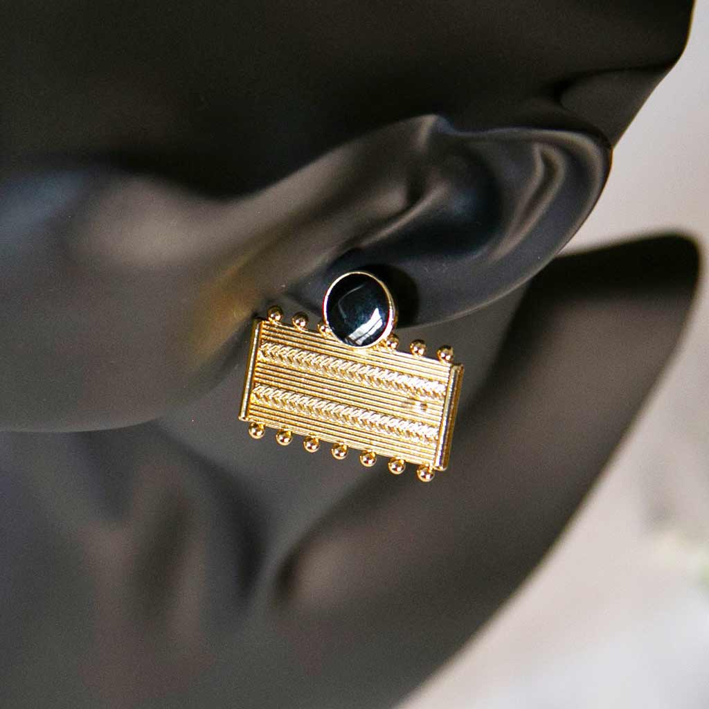 Tête de mannequin portant une boucle d'oreilles rectangulaires dorée et noire avec des motifs géométrique