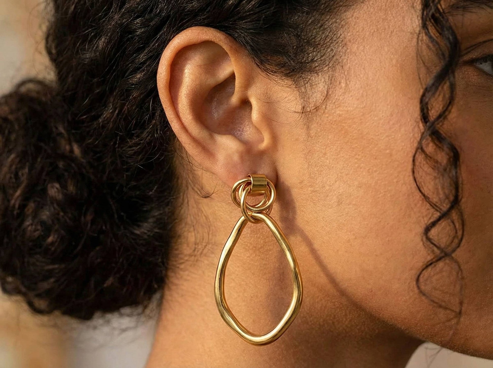 Jeune femme portant des boucles d’oreilles pendantes dorées ovales irrégulières en acier inoxydable – bijou élégant Lidiar Collection