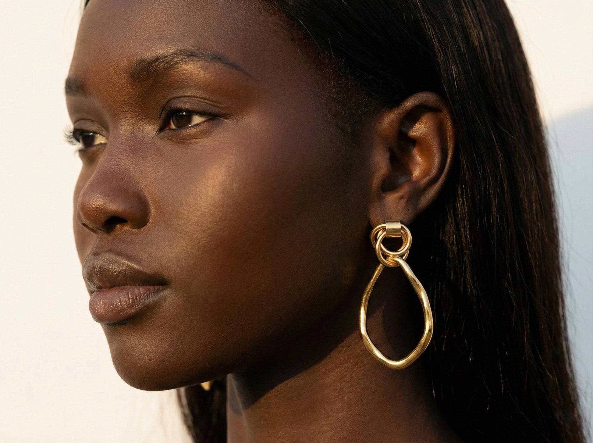 Jeune femme portant des boucles d’oreilles pendantes dorées ovales irrégulières en acier inoxydable – bijou élégant Lidiar Collection