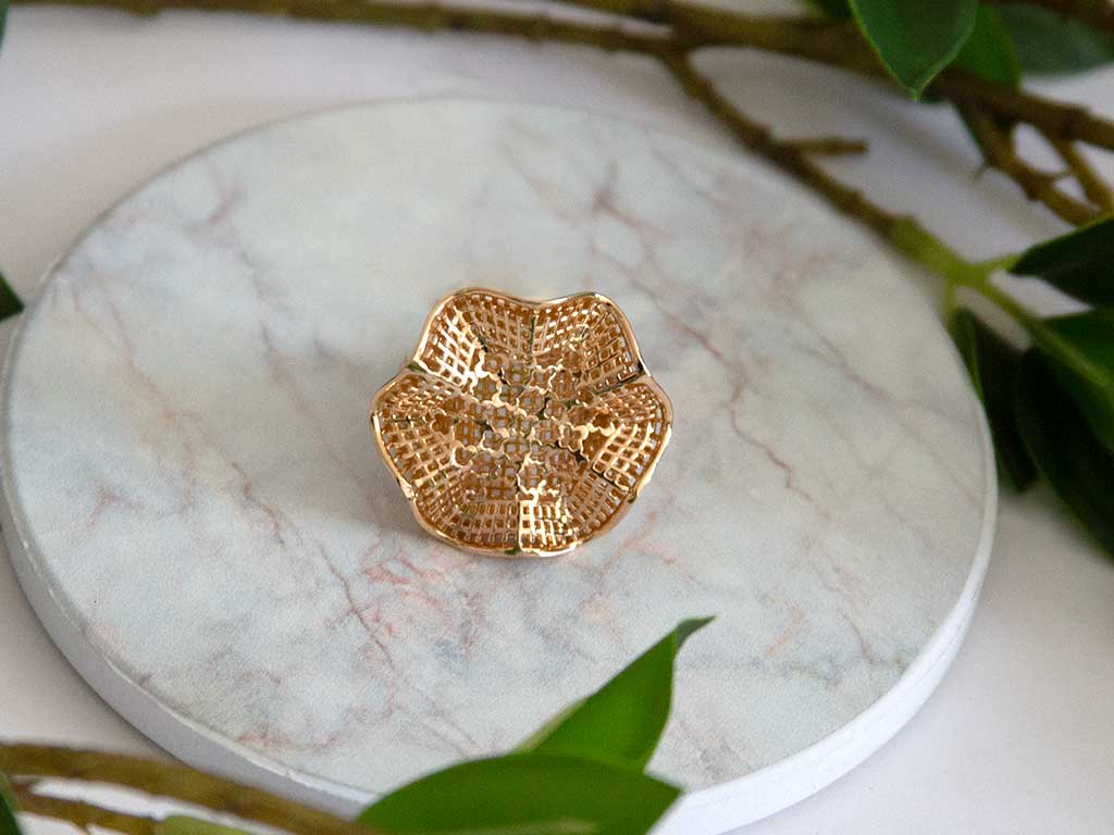 bague dorée en forme de fleure posée sur un plateau en marbre