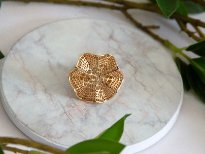 bague dorée en forme de fleure posée sur un plateau en marbre