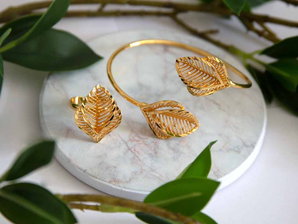 un bracelet et une bague bague en forme de feuille posés sur un plateau de marbre avec des plantes vertes en décor