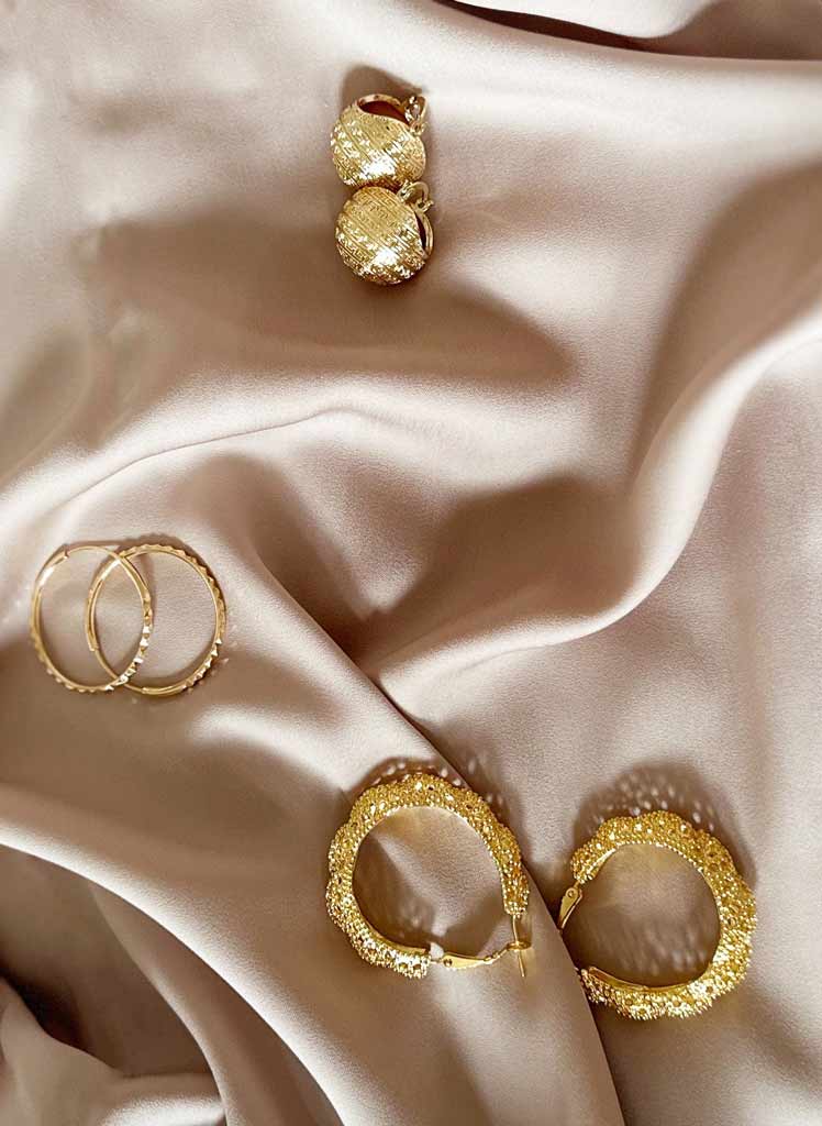 Quatre boucles d'oreilles dorées posées sur un tissu satiné beige