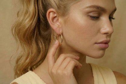 Jeune femme portant des Boucles d’oreilles créoles dorées fines en acier inoxydable, design minimaliste – Lidiar Collection