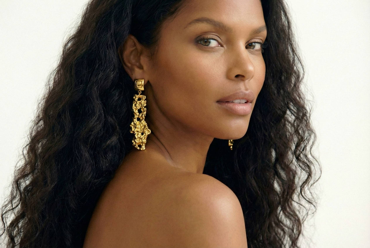 Jeune femme qui porte des boucles d'oreilles dorées effet martelé texturé en acier inoxydable - Modèle Siné par Lidiar Collection