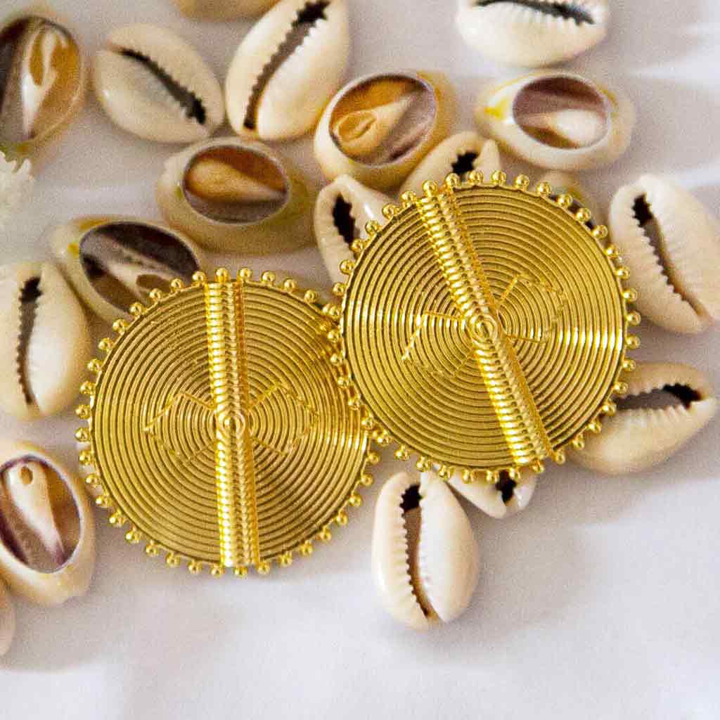 Boucles d'oreilles rondes ethniques dorées, posées sur des coquillages cauris