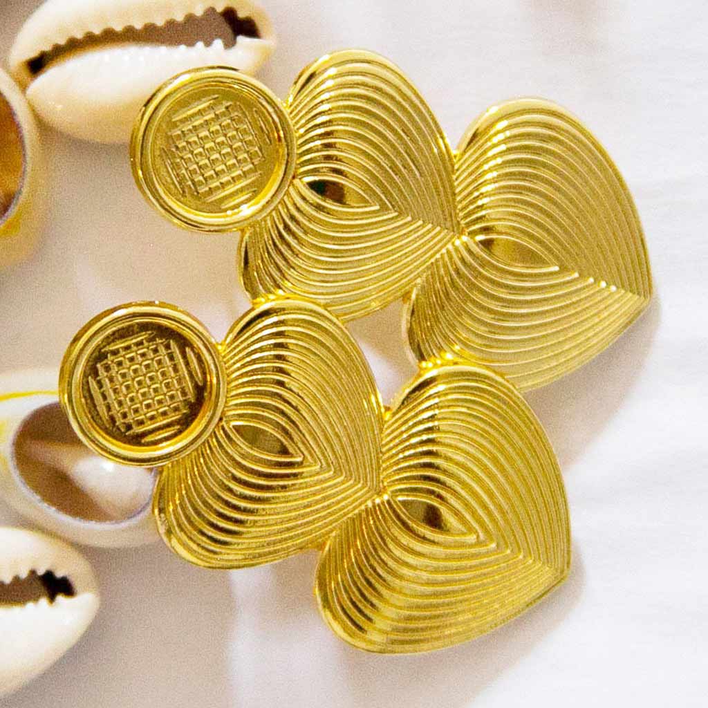 boucles d'oreilles longues en forme de coeurs, dorées posées sur des coquillages cauris 