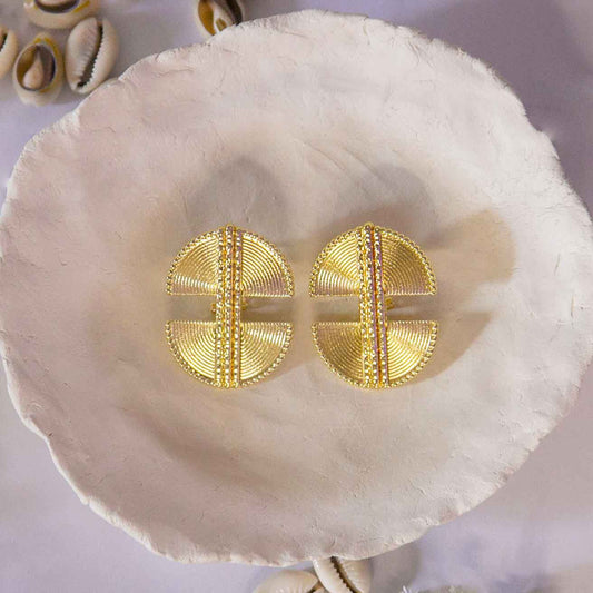 Boucles d'oreilles, style ethnique , dorée posées sur un plateau avec décor de coquillages cauris
