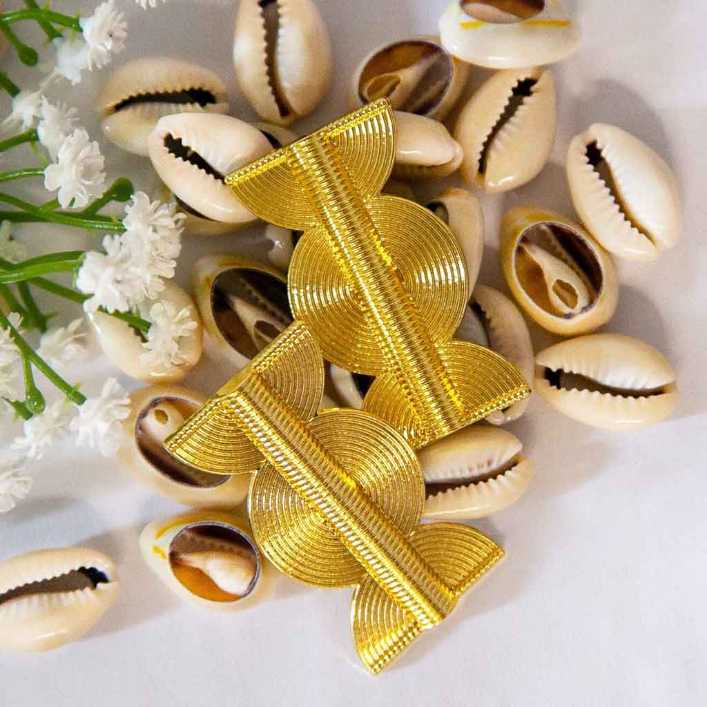 Boucles d'oreilles ethniques, dorées, posées sur des coquillages cauris et des fleures blanches en décor