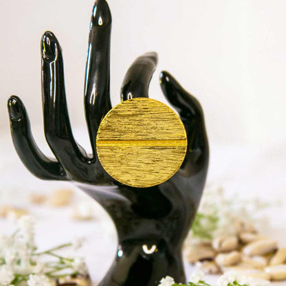 Main de mannequin portant une grosse bague ethnique en forme ronde , dorée au majeur, avec un décor de fleures blanches et de coquillages cauris