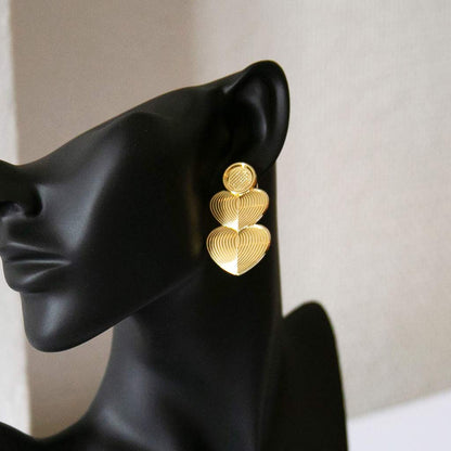 Tête de mannequin portant des boucles d'oreilles dorée, longues, en forme de coeur